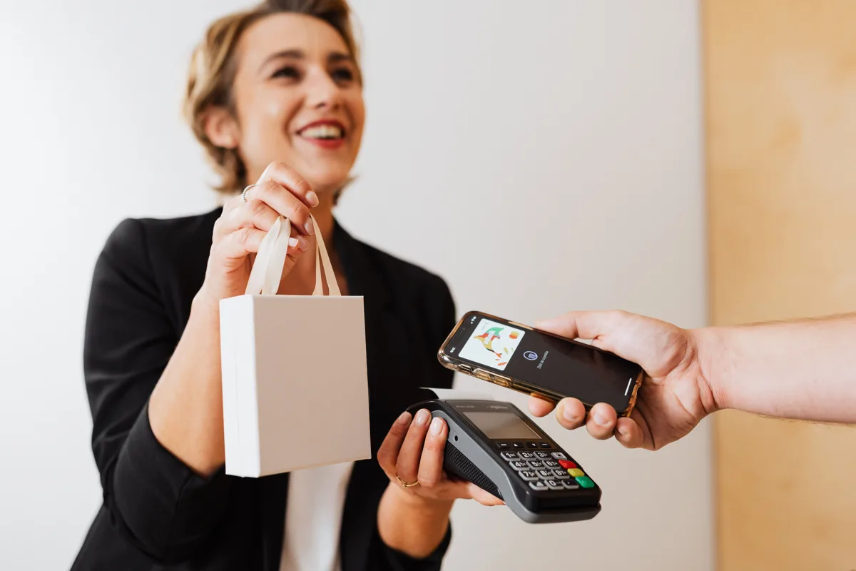 Cliente souriante qui règle ses achats avec son smartphone sur un terminal de paiement dans une boutique
