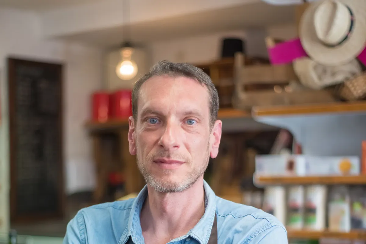 Commerçant en tablier derrière son comptoir dans une épicerie, les bras croisés