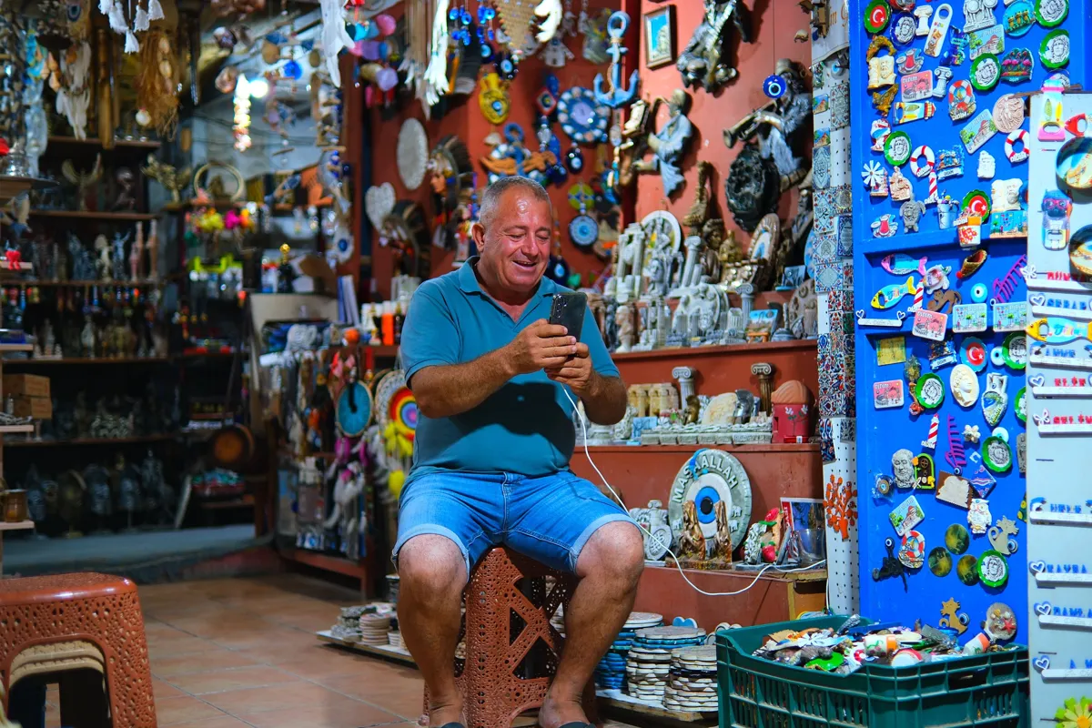 Commerçant souriant qui consulte son smartphone dans sa boutique de souvenirs