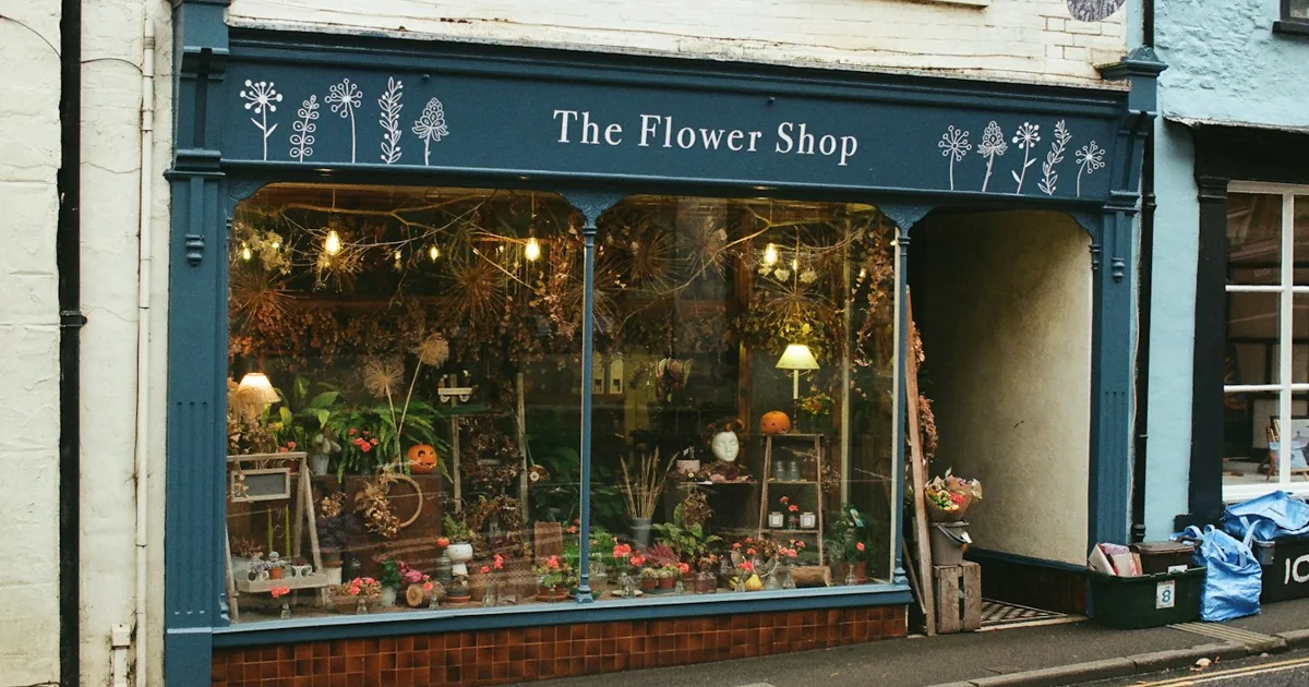 Vitrine d'une boutique de fleurs en rue, avec son enseigne bleue et ses plantes séchées exposées derrière la vitre