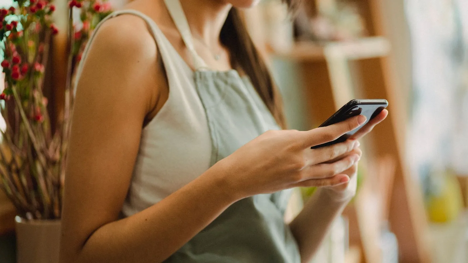 Fleuriste en tablier qui consulte sa fiche sur son smartphone, à côté d'un bouquet de baies rouges dans sa boutique