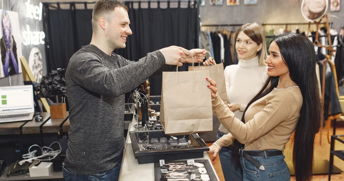 Commercant souriant remettant des sacs a deux clientes satisfaites au comptoir