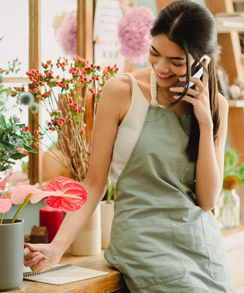 Fleuriste souriante qui prend un appel et note la commande dans un cahier