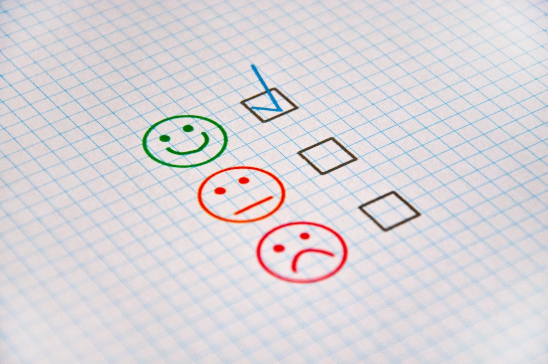 Customer giving satisfaction feedback with positive, neutral and negative rating icons on a questionnaire.
