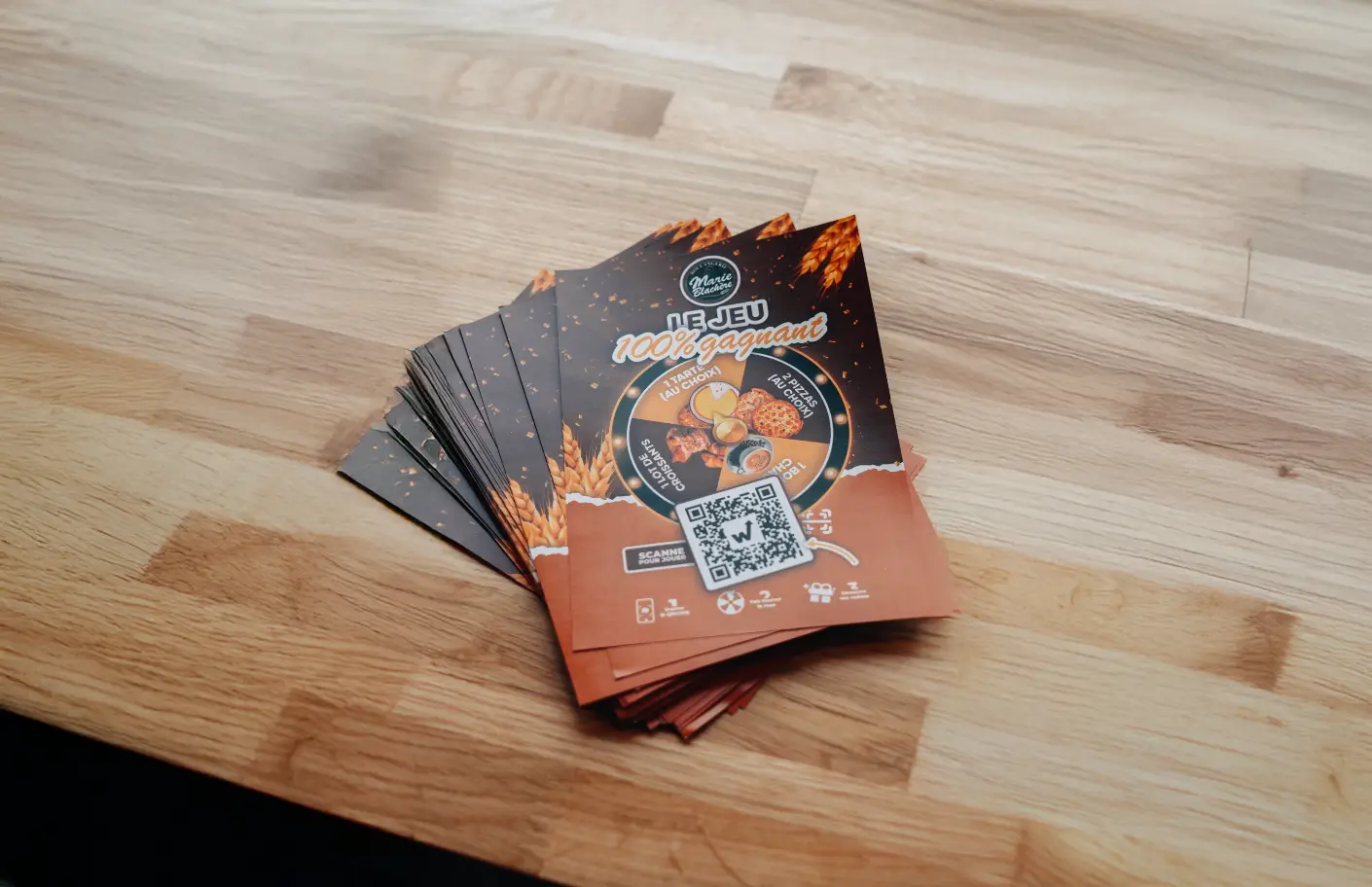 Marie Blachère 100% winning game flyers with prize wheel and QR code spread out on a wooden table